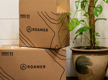 Two Roamer storage boxes stacked on top of one another next to a plant.
