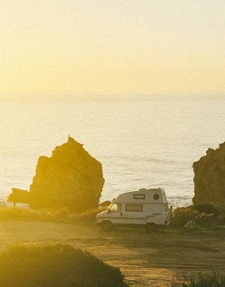 A campervan parked up next to a beach watching the sunrise.