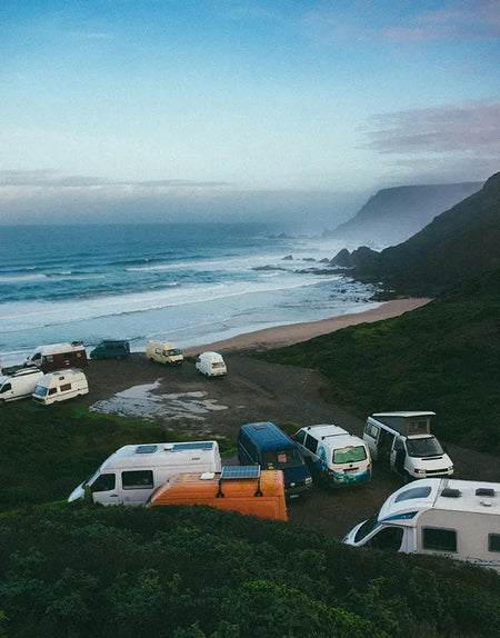 A crowd of campervans and motorhomes parked next to a beach.