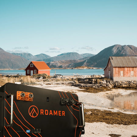 Roamer's home battery superimposed onto a beach next to two off grid houses.