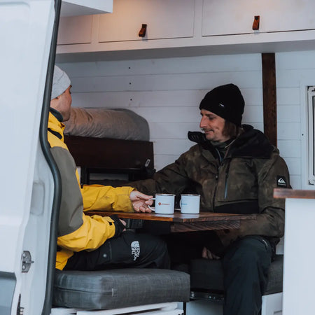 Professional speedriders Valentin Delluc and Ugo Gerola sat inside Roamer's campervan, Chewie. They are enjoying a coffee in Roamer branded mugs.
