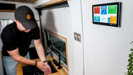 Steve Kennedy from Roamer batteries washing his hands in a Roamer campervan. A digital monitor screen displaying Victron energy and Roamer battery status.
