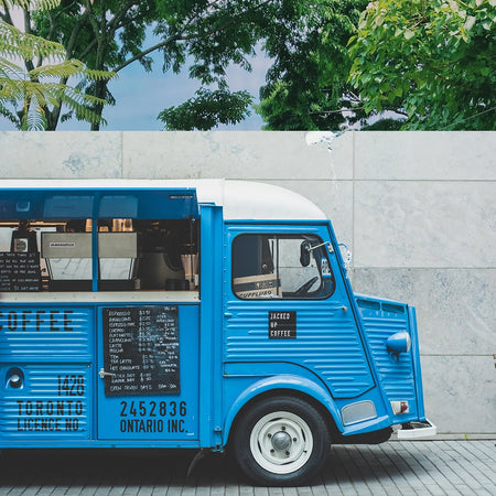 A blue coffee wagon parked up against a grey wall ready to serve customers.