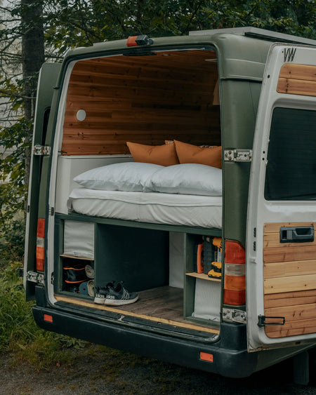 A green sprinter Campervan parked up with its doors open.